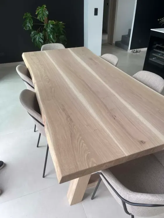 Table de repas en bois massif clair avec chaises, devant une baie vitrée