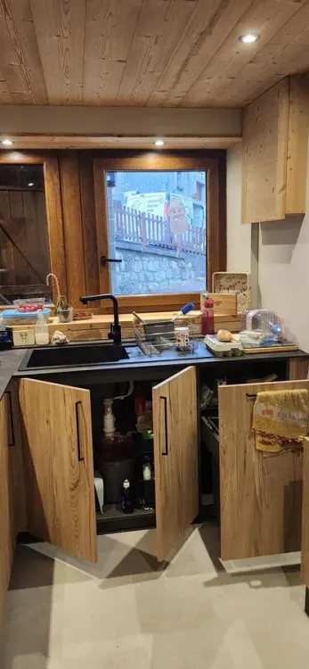 Cuisine en vieux bois avec évier noir et rangements ouverts devant la fenêtre