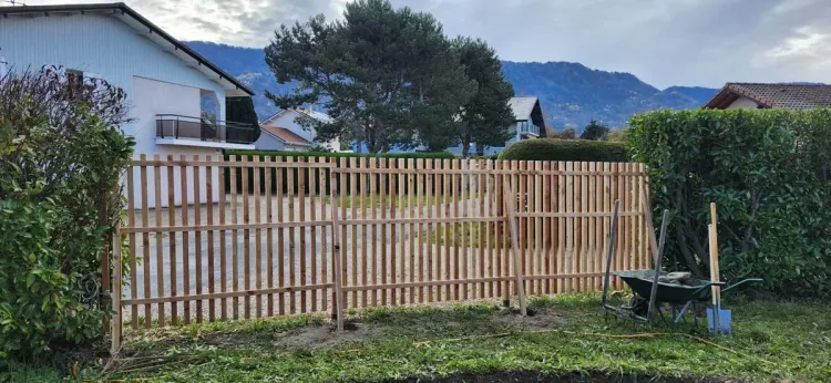 Clôture en bois ajourée délimitant un jardin, avec vue sur les montagnes