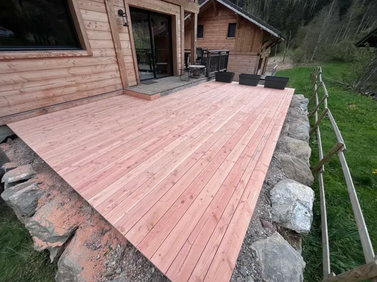 Terrasse en bois neuve avec emmarchement en pierre le long d’un chalet